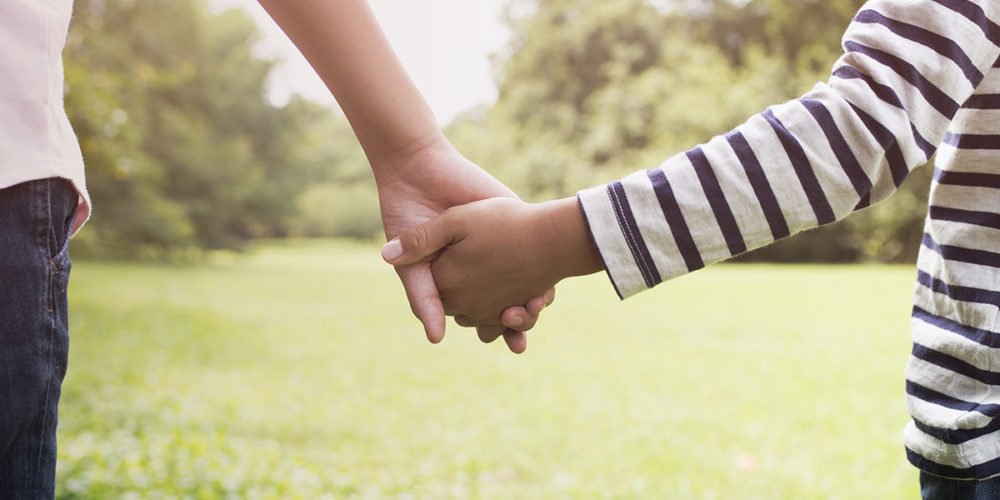 Two children holding hands as they walk in a park.