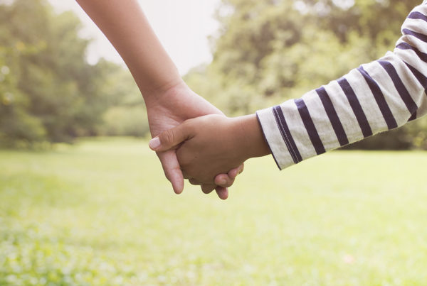 Two children holding hands as they walk in a park.