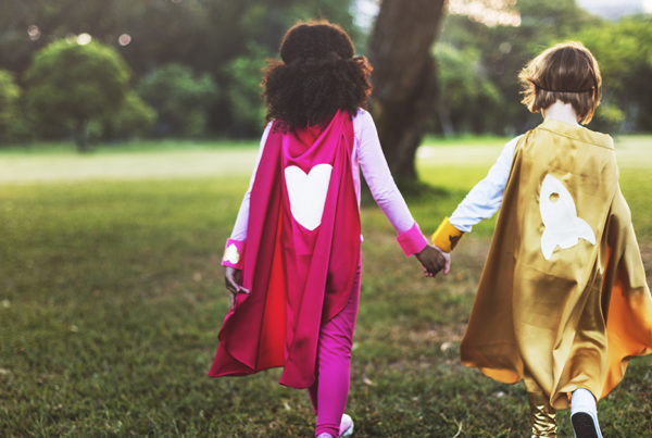 Two children wearing homemade superhero caps and holding hands.