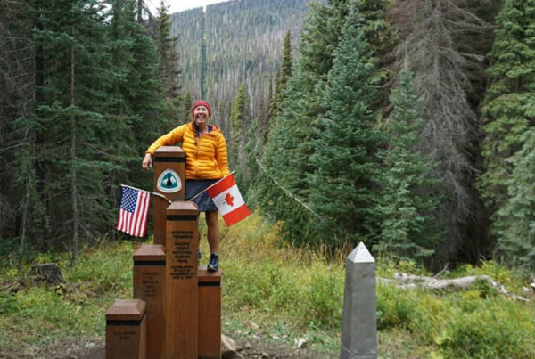 Hiker standing next to posts indicating it's the U.S.-Canada border.