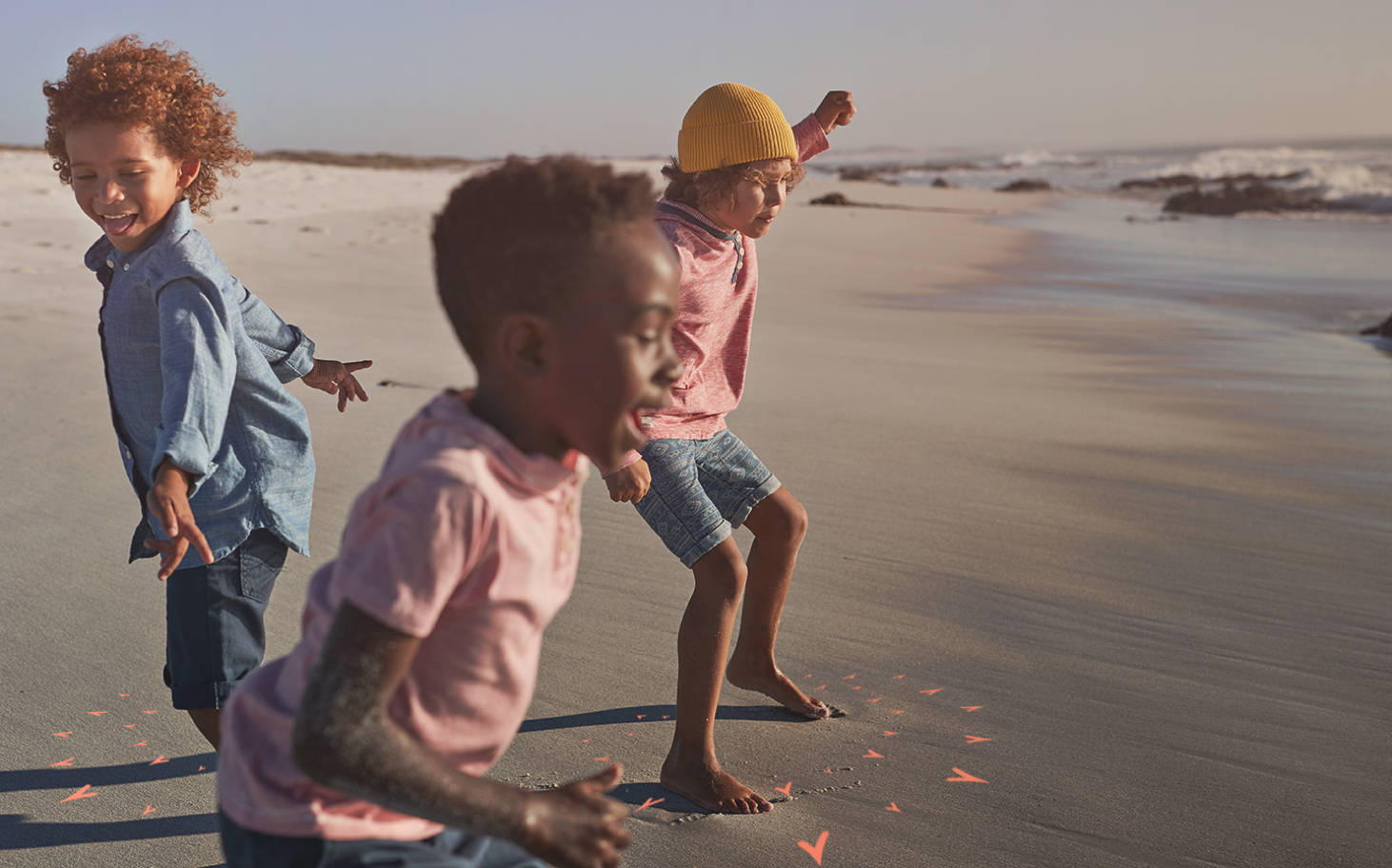 Three children playing on the beach at the water's edge.