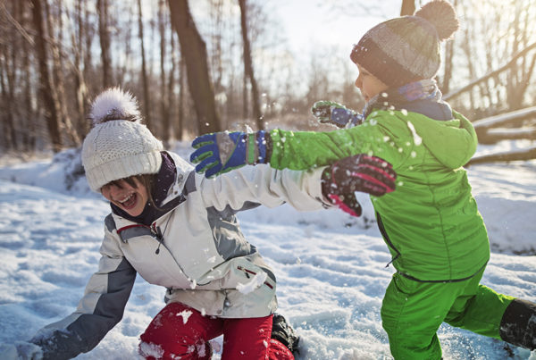 Two kids playing snowball fight in winter forest