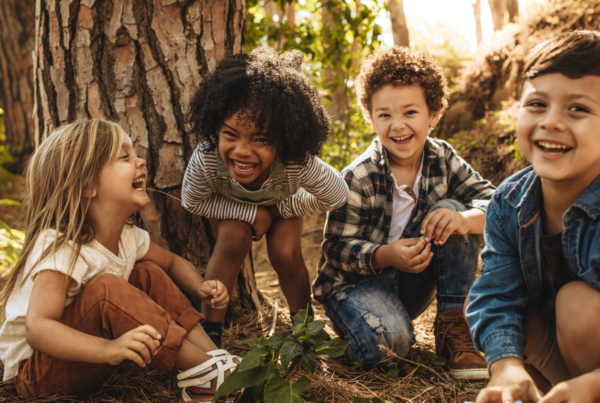 Four young kids sitting on the ground next to a large tree.