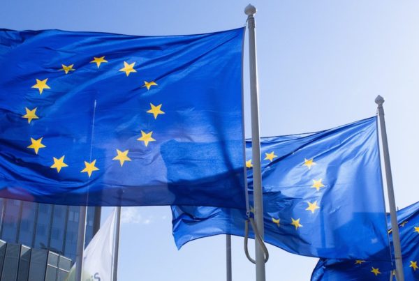 Three European Union flags fluttering at the top of three flag poles.