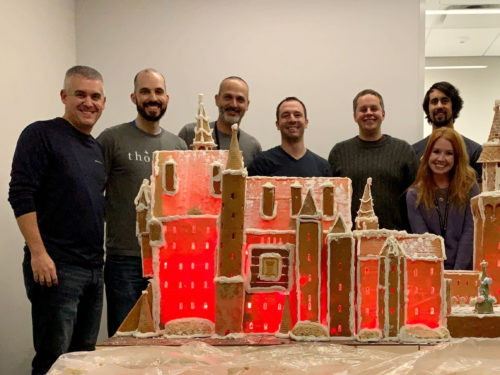 Group of employees pictures with an elaborate gingerbread house displayed in front of them.