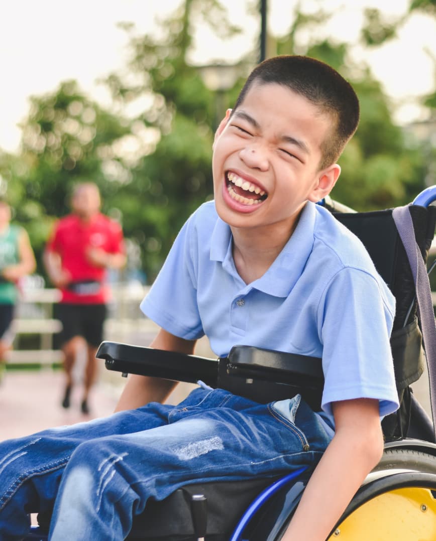 A young boy in a wheelchair laughs and makes faces for the camera.