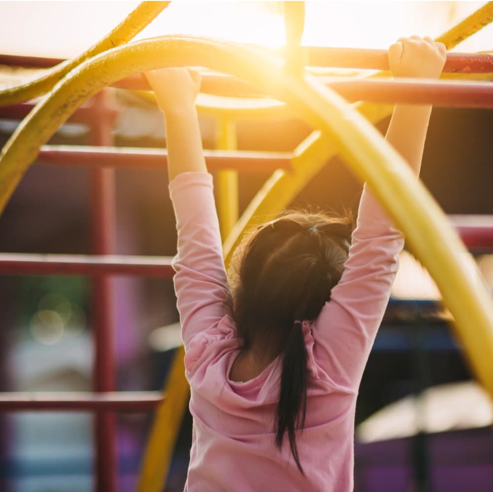 A young girl plays on a set of monkeybars at sunset.