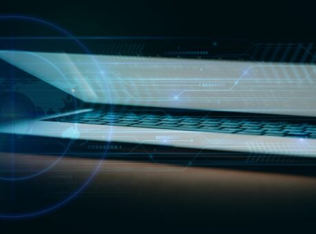 Glow from a partially closed laptop illuminates a dark room.